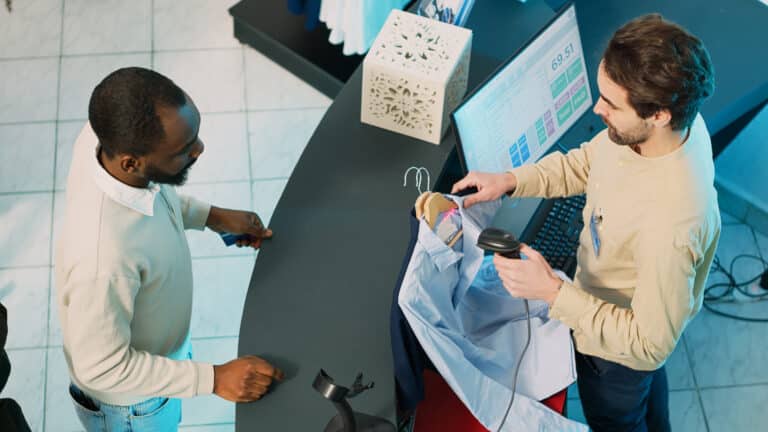 african-american-man-buying-clothes-shop-cash-register-using-card-make-transaction-pos-terminal-store-employee-removing ERs tag which is an anti theft device on cloth