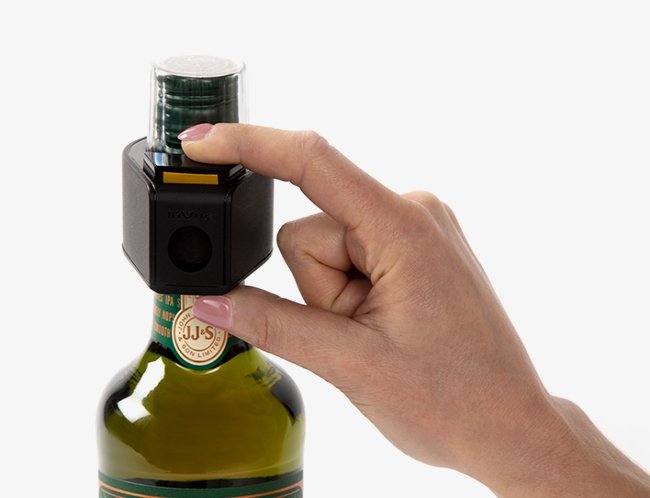 A hand is shown with a bottle cap to unlock a wine bottle tag from the top of a bottle.