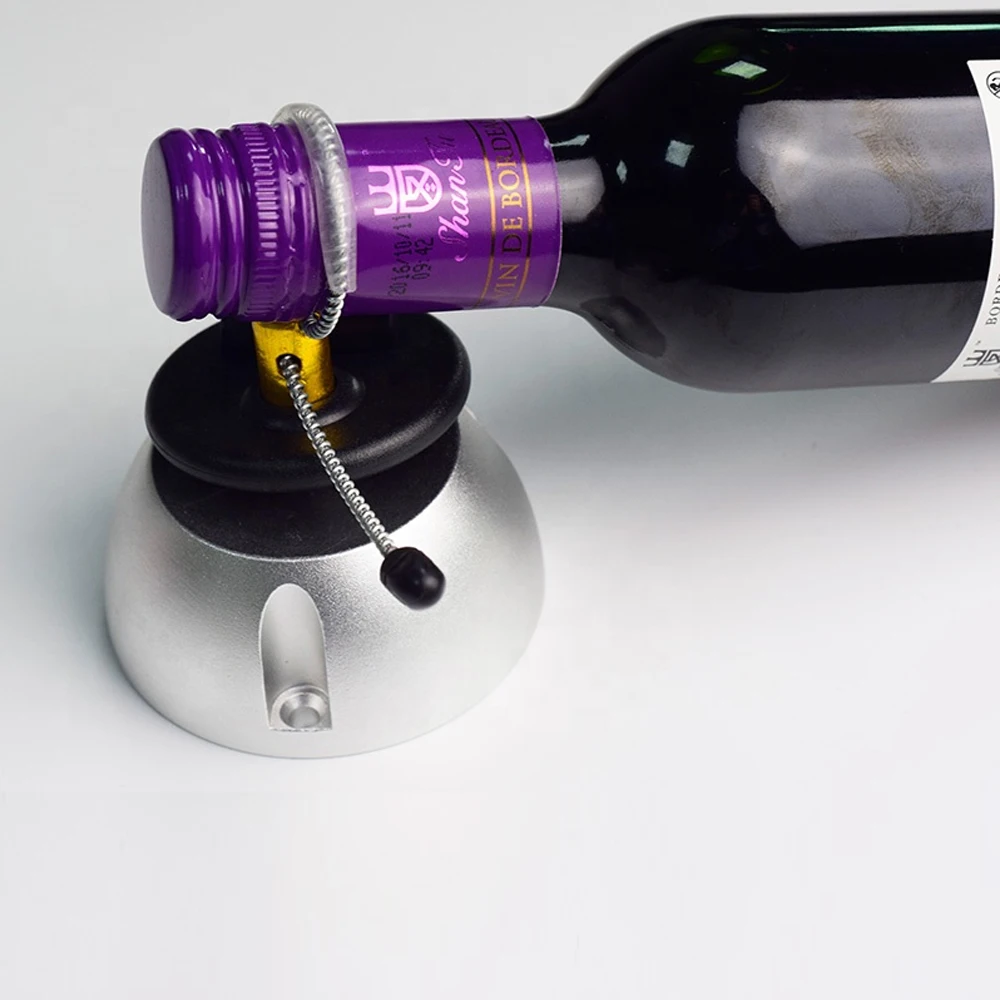 A wine bottle with a purple capsule and label is secured with some wine bottle tags attached to its neck. The tag is connected to a silver, round base with a black button.